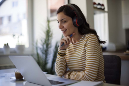 Young woman with bluetooth headphones attending an online class on her laptop