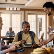 Young caregiver serving a glass of water to senior people during lunch in nursing home.